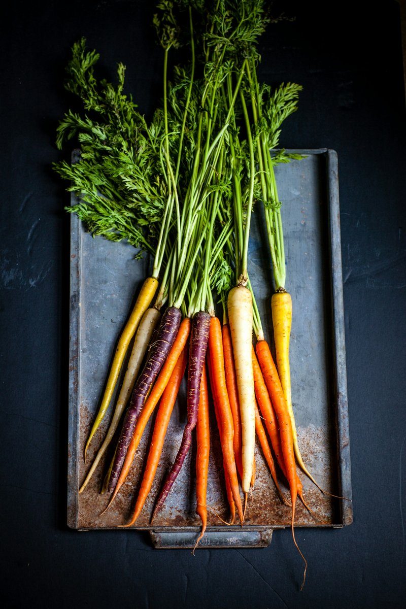 Carottes de couleurs avec leurs fanes posées sur un plateau
