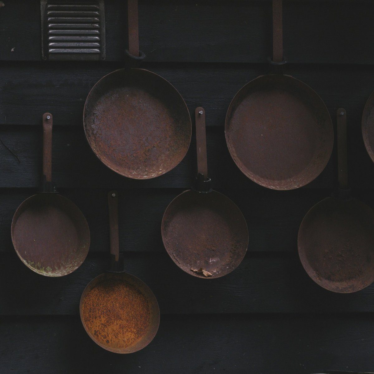 Vieilles poêles et casseroles accrochées à un mur sombre